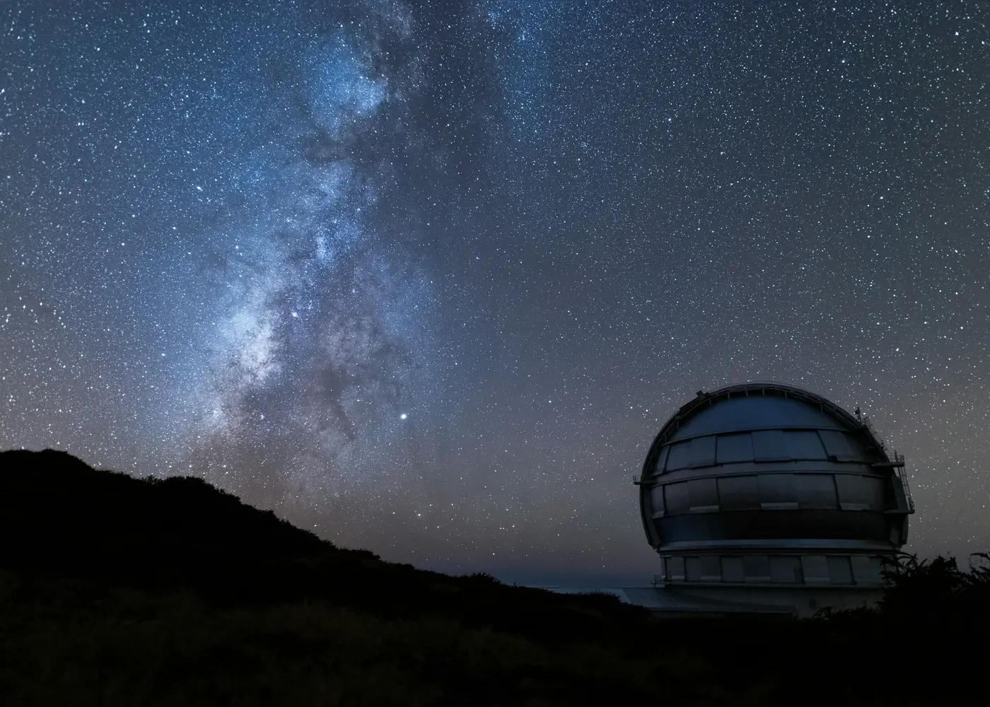 A telescope dome on a hill under the Milky Way